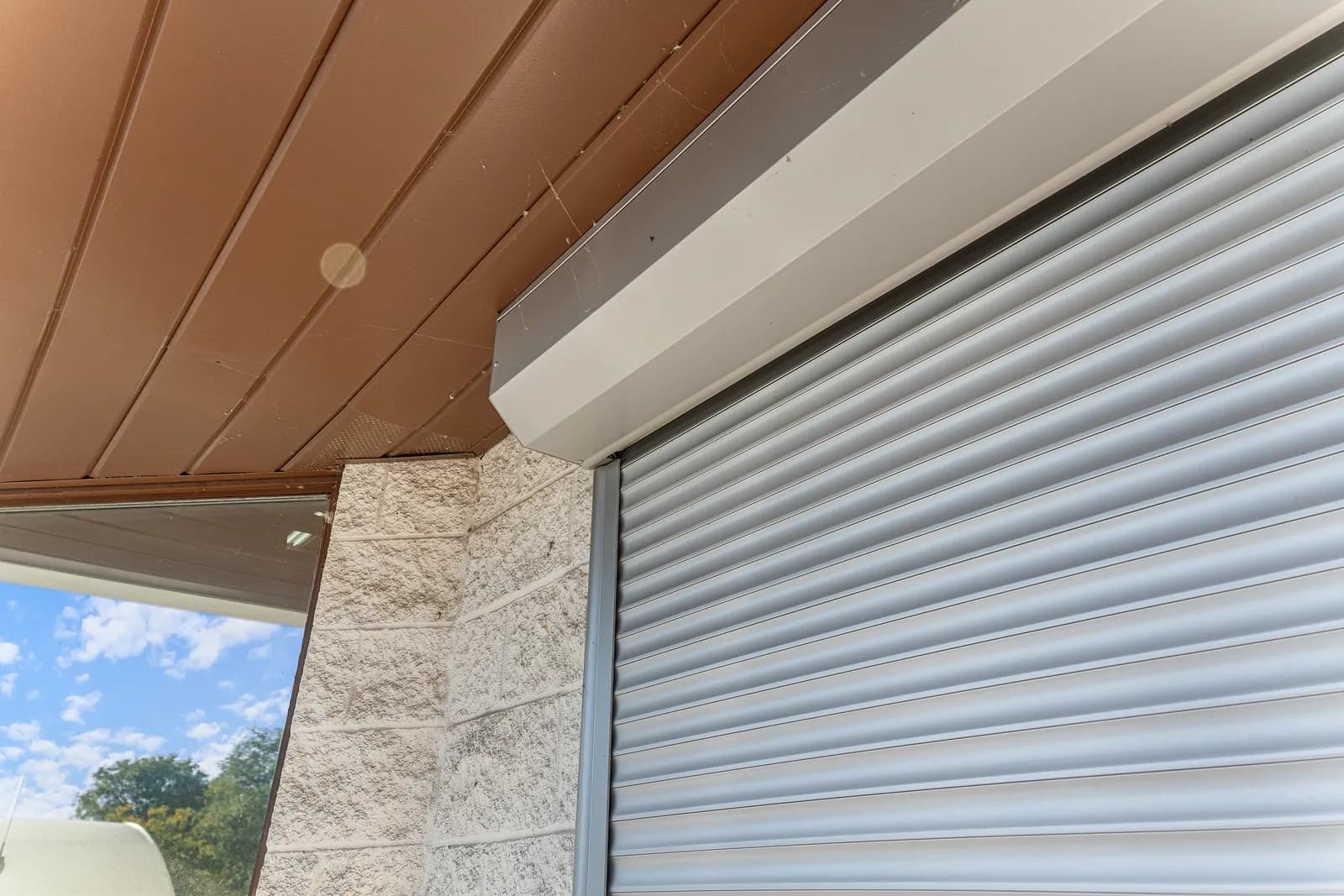 Backyard pool framed through a residential home with roll shutters on the deployed back facade