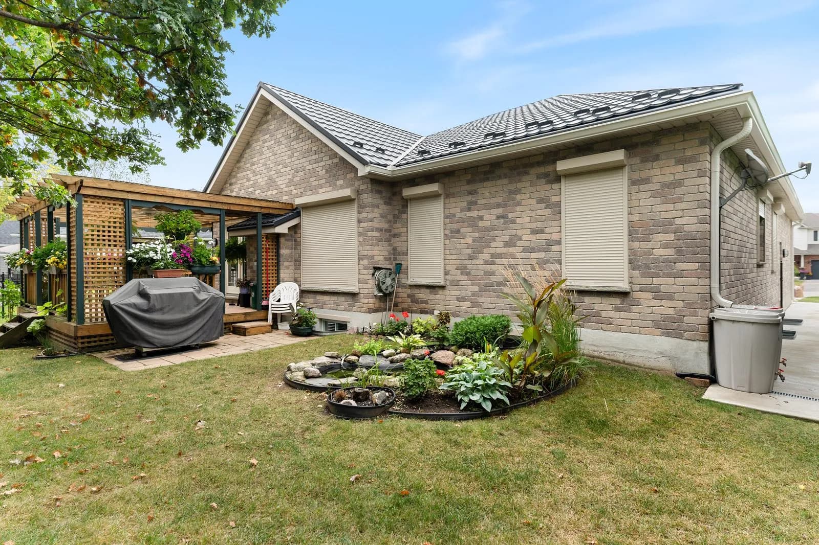 Suburban Ontario brick home with cream aluminum roll shutters retracted, pergola in the yard