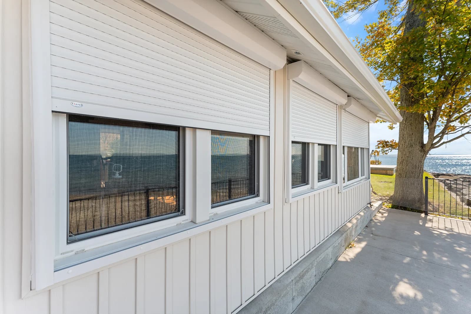 White Ontario lake home with cream aluminum roll shutters retracted above the windows