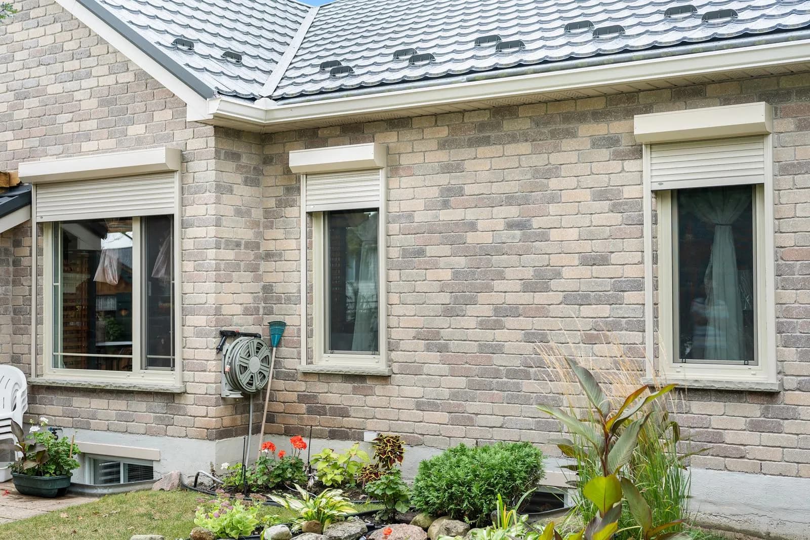 Brick bungalow side elevation with cream aluminum roll shutters retracted above three windows