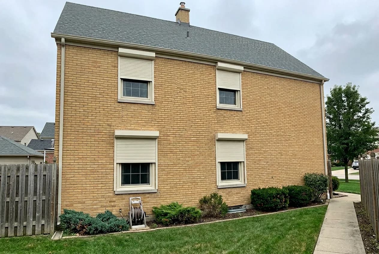 Buff-brick Ontario home side elevation with four cream aluminum roll shutters deployed over the side windows