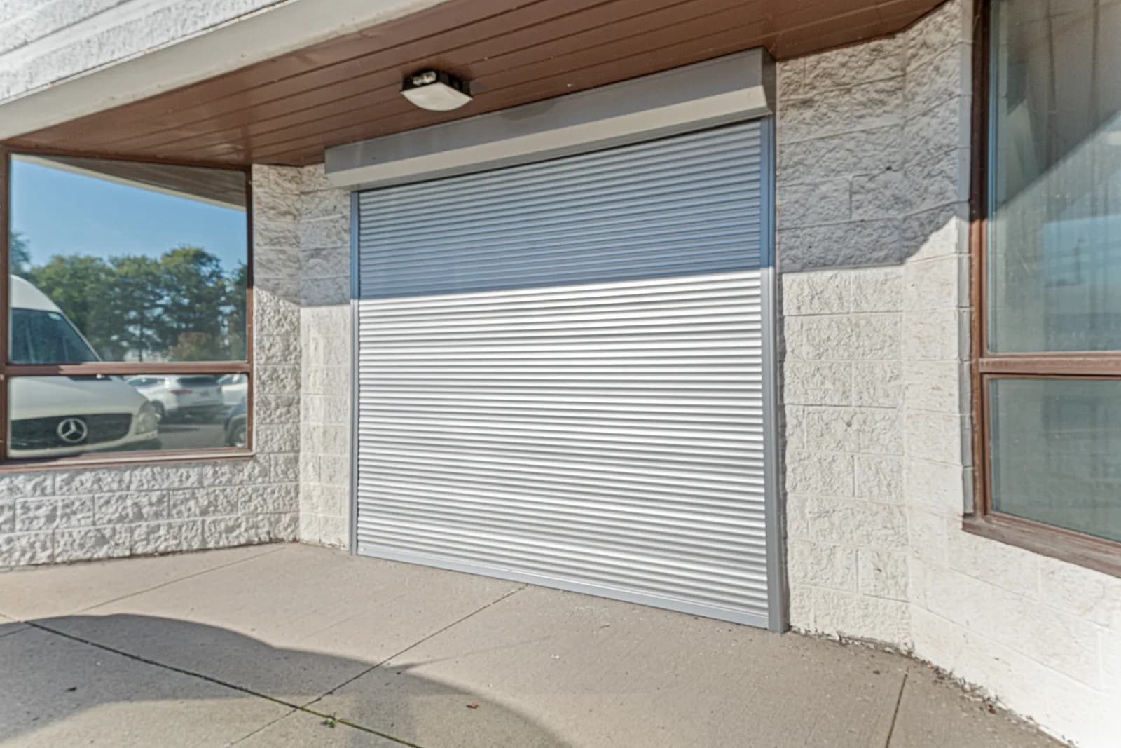 Commercial storefront with a wide silver aluminum roll shutter half-deployed over a glass entrance