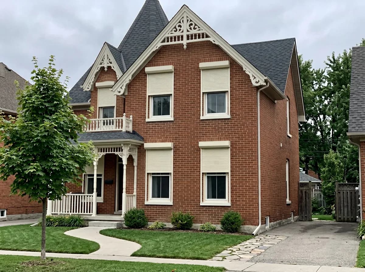 Two-story red-brick Victorian Ontario home with cream aluminum roll shutters deployed over four front windows