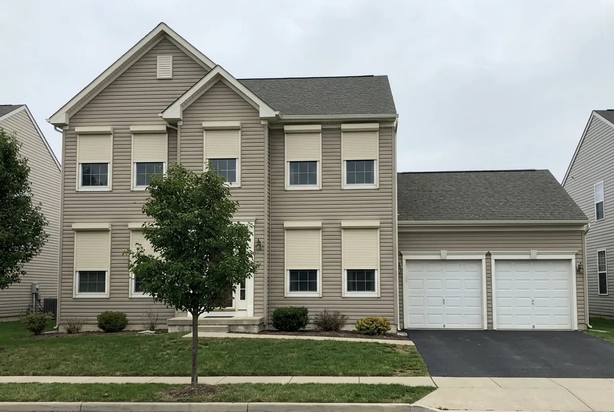 Two-story beige vinyl Ontario home with cream aluminum roll shutters deployed across multiple front windows