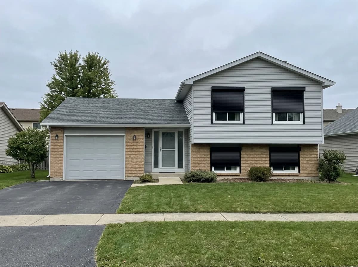 1970s grey vinyl split-level Ontario home with four black aluminum roll shutters deployed across the front windows