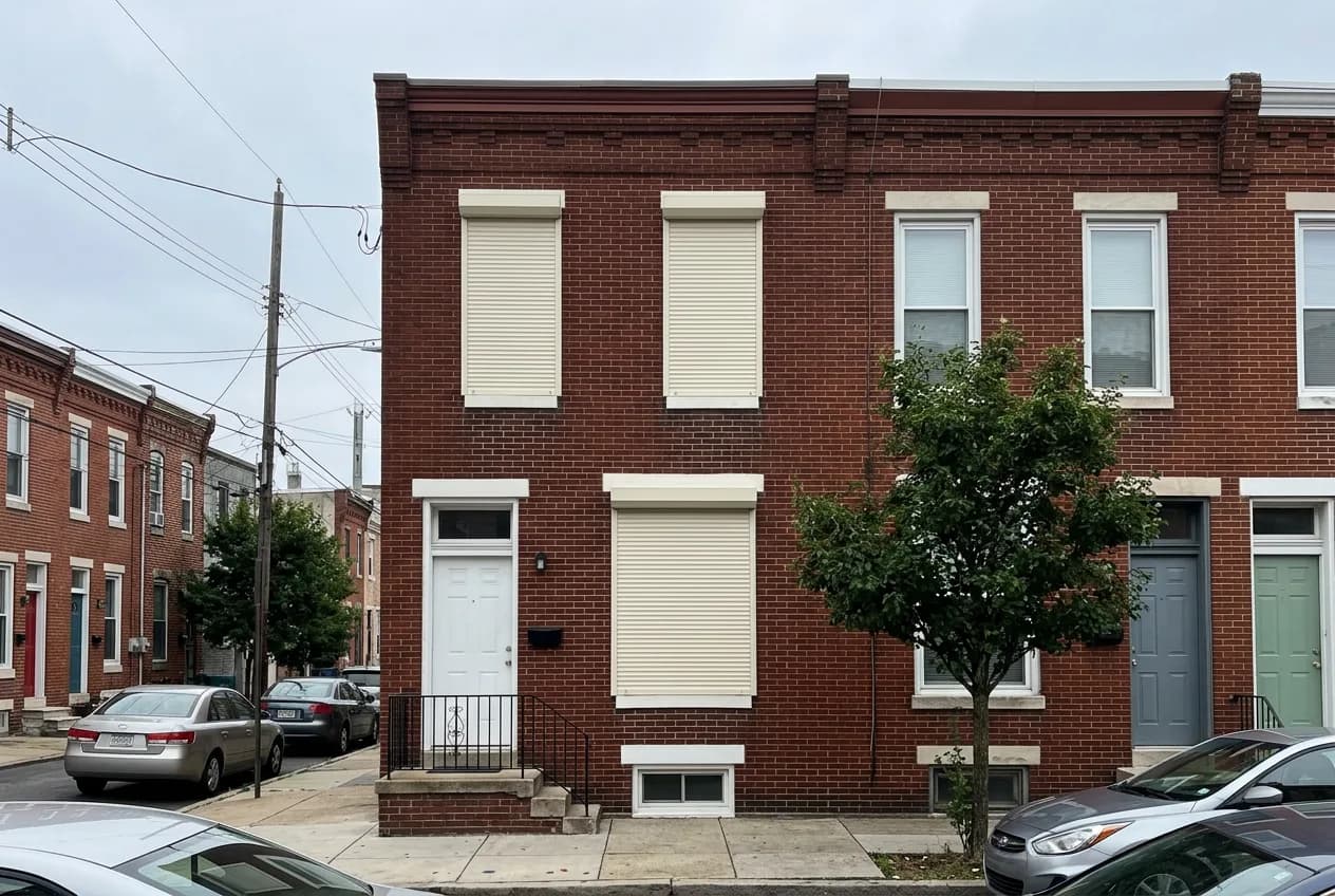 Red-brick urban Ontario row house with three cream aluminum roll shutters deployed over the front windows
