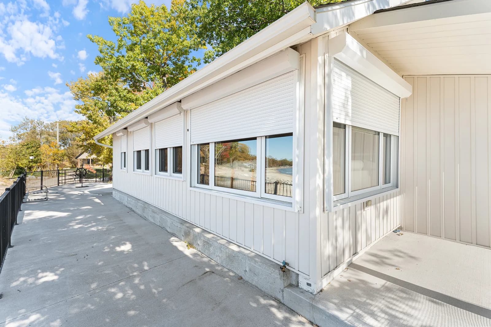 White-clad lake home side elevation with cream aluminum roll shutters retracted above the windows