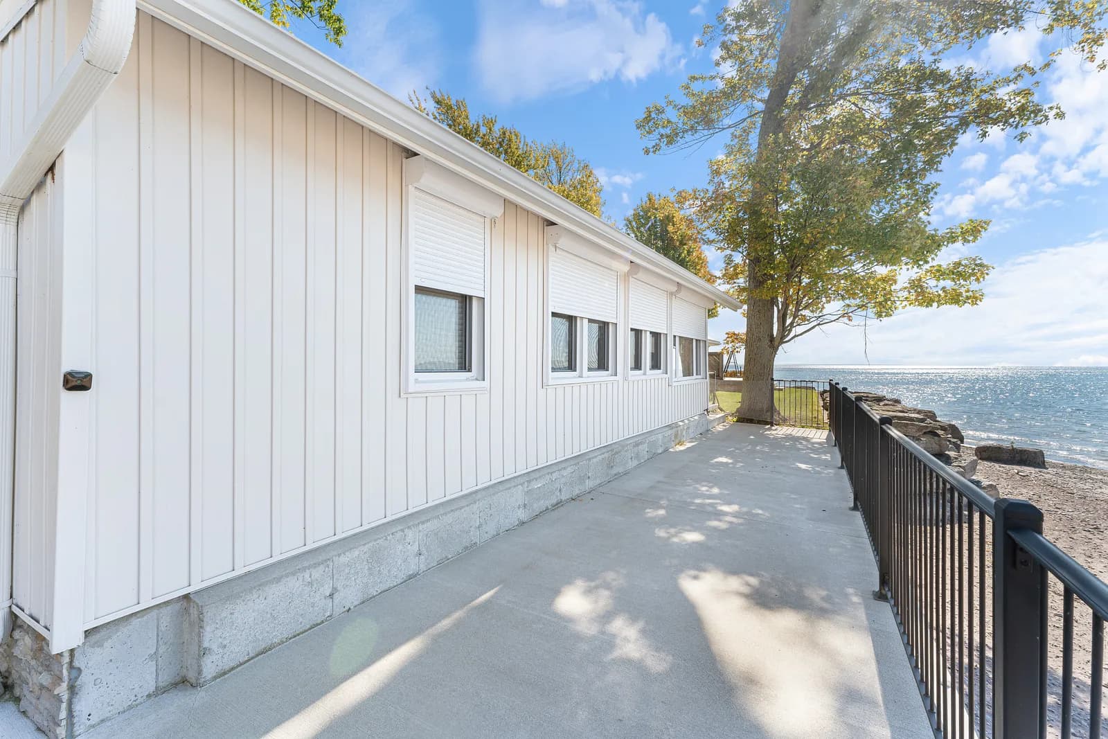 White-clad lake home side walkway with a single aluminum roll shutter visible on the wall